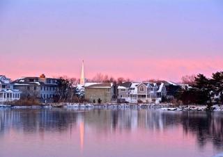 houses covered in snow on the water with a pink sky